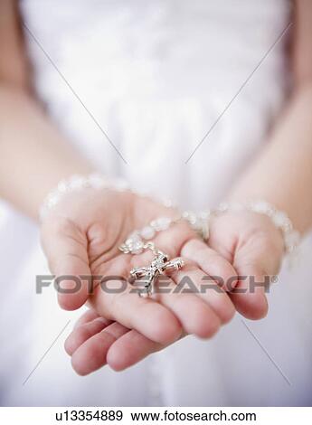Stock Photo - Close up of girl's (8-9) hands holding rosary beads. Fotosearch