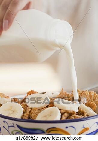 Stock Photo - Close up of hand pouring milk into bowl of cereals. Fotosearch