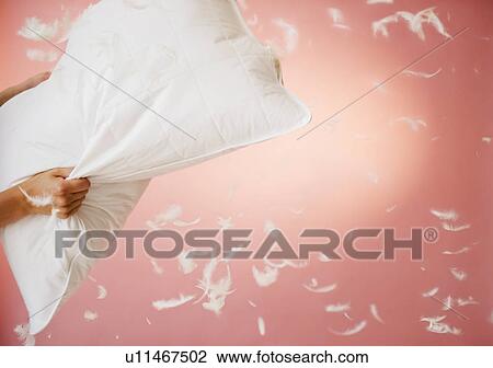 Stock Image - Close up of hands holding pillow with feathers flying around. Fotosearch