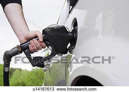 Stock Image - Close up of man's hand holding fuel pump and refueling car. Fotosearch