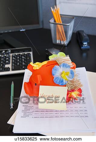 Stock Photography - Close up of piggy bank and lei on desk in office. Fotosearch