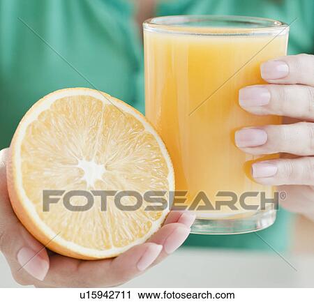 Stock Image - Close up of woman's hands holding half of orange and glass of juice. Fotosearch