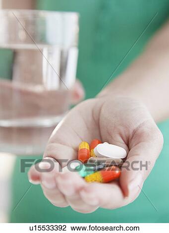 Stock Image - Close up of woman's hands holding pile of medicines. Fotosearch