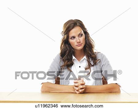 Stock Photograph - Concerned business woman sitting at table with hands clasped. Fotosearch