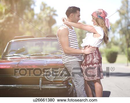 Stock Image - Couple embracing near convertible car. Fotosearch