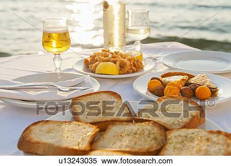 Stock Photography - Greece, Cyclades Islands, Mykonos, Calamari appetizer on set table by sea. Fotosearch