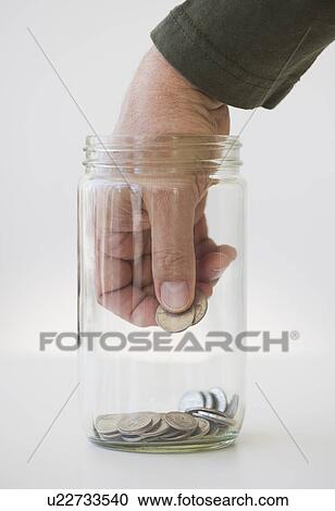 Stock Image - Hand inserting coin into jar. Fotosearch