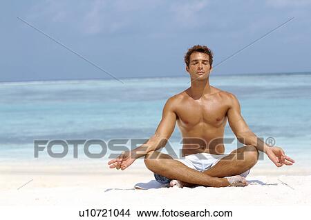 Handsome young man meditating in a lotus position on the beach View Large Photo Image Picture - Handsome young man meditating in a lotus position on the beach. Fotosearch