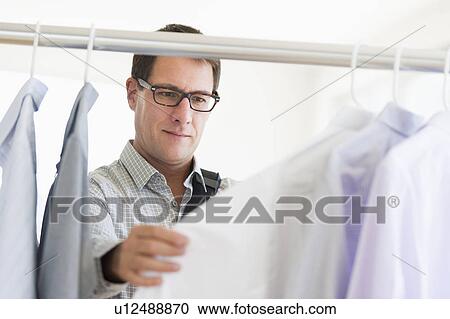 Stock Image - Man choosing shirts in store. Fotosearch