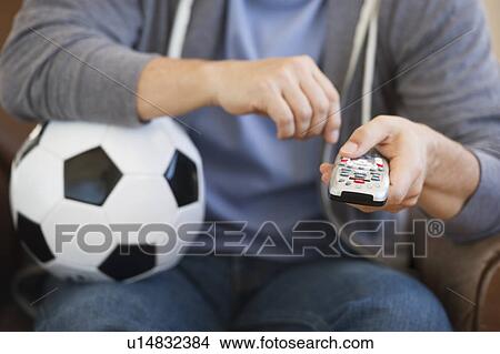 Picture - Man holding soccer ball and remote control. Fotosearch