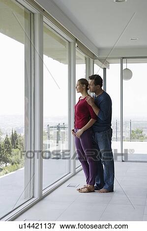 Stock Photo - Mature couple in empty living room looking through window. Fotosearch