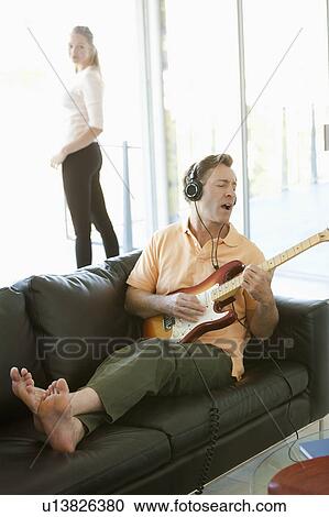 Stock Image - Mature man playing guitar woman standing next to window. Fotosearch