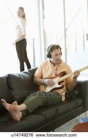 Stock Photograph - Mature man playing guitar woman standing next to window. Fotosearch
