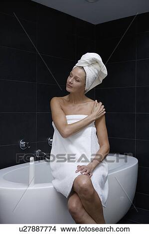 Picture - Mature woman sitting in bathroom wrapped in towel. Fotosearch