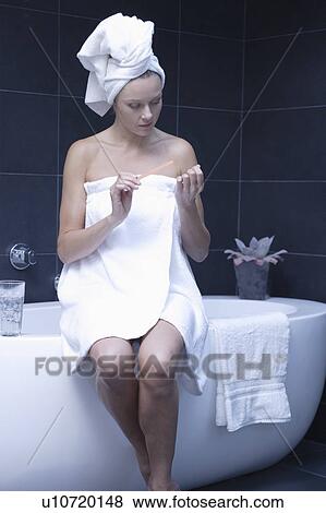 Stock Photo - Mature woman sitting in bathroom wrapped in towel. Fotosearch