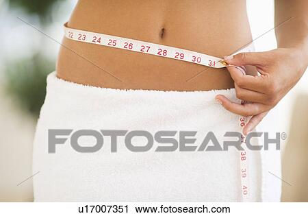 Stock Image - Midsection of woman measuring waist. Fotosearch
