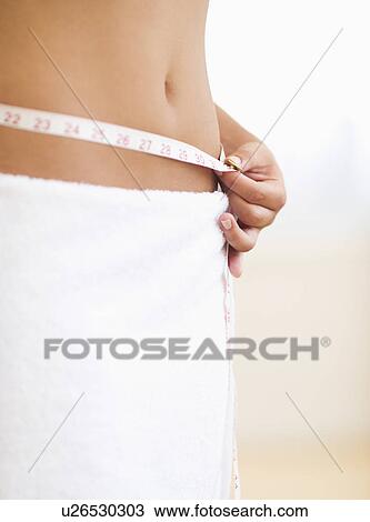 Stock Image - Midsection of woman measuring waist. Fotosearch