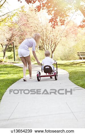 Stock Photo - Mother and son (2-3) riding tricycle in park. Fotosearch