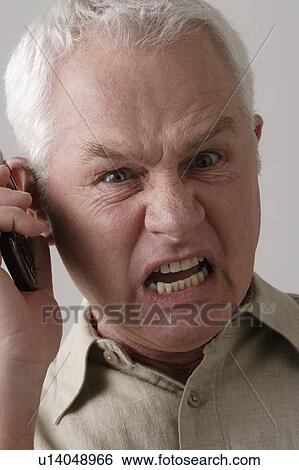 Stock Photograph - Portrait of angry senior man with mobile phone, studio shot. Fotosearch