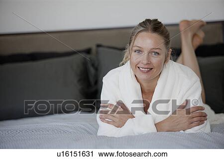 Stock Image - Portrait of mature woman lying on bed. Fotosearch