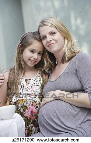 Stock Image - Portrait of pregnant mother and daughter (6-7)embracing. Fotosearch