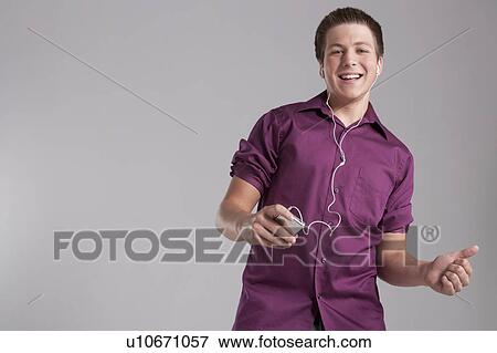 Stock Photo - Portrait of smiling teenager listening mp3 player, studio shot. Fotosearch