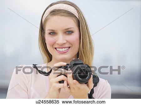Stock Photography - Portrait of young woman holding camera, smiling. Fotosearch