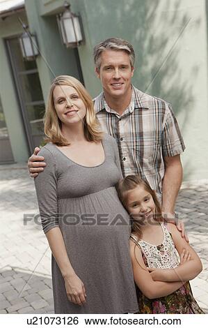 Stock Photograph - Pregnant mother, father and daughter (6-7) posing for portrait. Fotosearch
