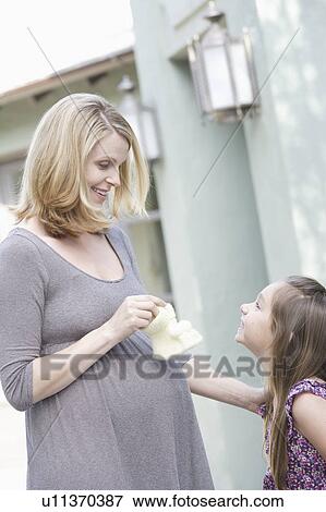 Stock Photo - Pregnant mother holding baby booties standing with daughter (6-7) . Fotosearch