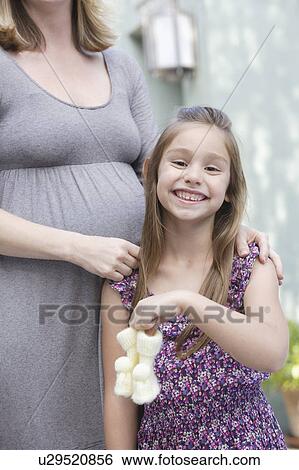 Stock Photograph - Pregnant mother standing with daughter (6-7) holding baby booties . Fotosearch