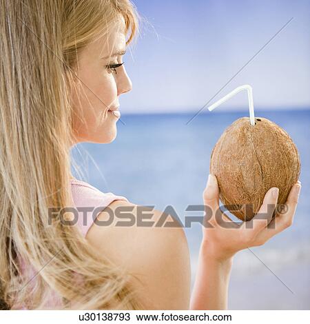 Stock Image - Profile of woman holding coconut with straw. Fotosearch