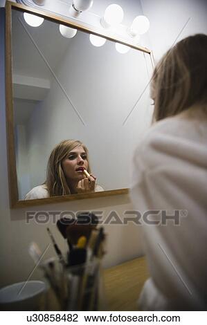 Stock Image - Reflection in mirror of woman doing make up. Fotosearch