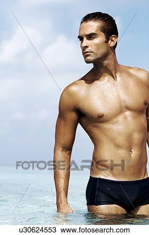 Sexy young man in swim trunks standing in the sea View Large Photo Image Stock Image - Sexy young man in swim trunks standing in the sea. Fotosearch