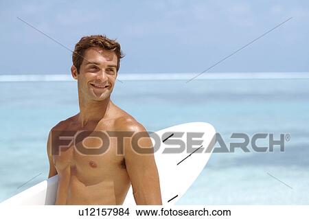 Picture - Shirtless young man holding surfboard. Fotosearch