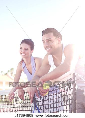 Stock Photo - Smiling couple standing near tennis net. Fotosearch