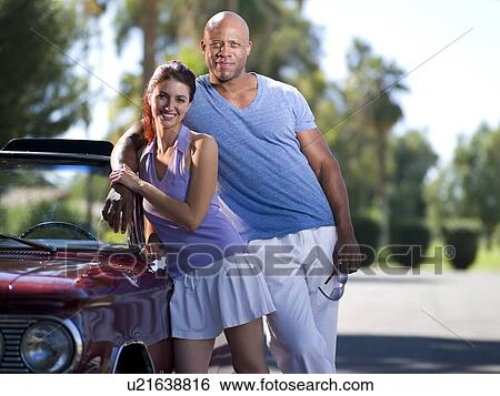 Stock Photograph - Smiling couple standing together near classic's car. Fotosearch