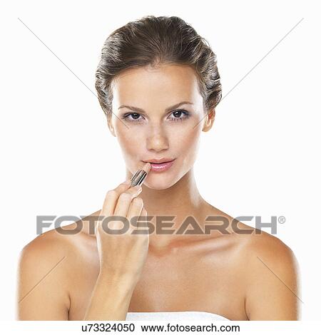 Stock Image - Studio portrait of beautiful woman applying lipstick. Fotosearch