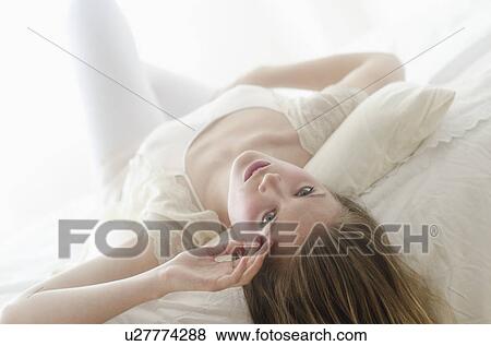 Stock Photo - Studio portrait of young woman lying on bed. Fotosearch