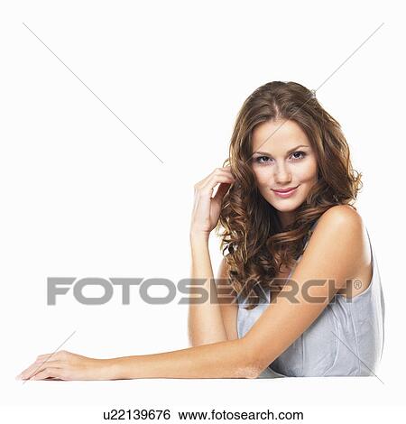 Stock Photograph - Studio portrait of young woman sitting at table and smiling. Fotosearch