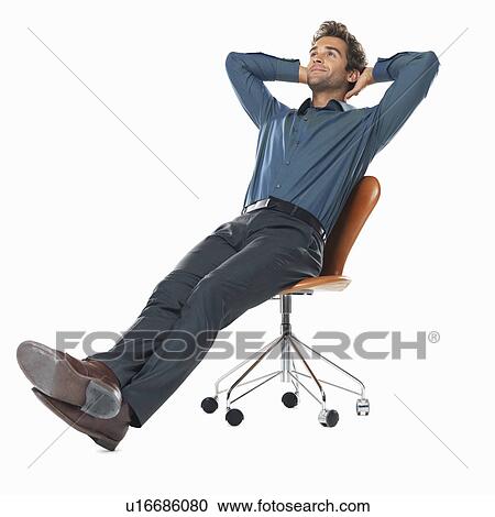 Stock Image - Studio shot of young business man relaxing on chair with hands behind head. Fotosearch