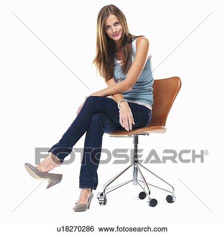 Stock Photograph - Studio shot of young woman sitting on chair with legs crossed. Fotosearch