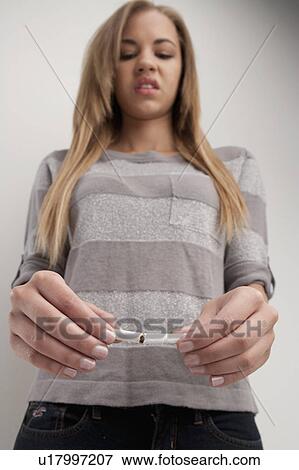 Stock Photo - Teenage girl (16-17) breaking cigarette, studio shot. Fotosearch
