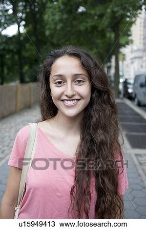 Stock Image - USA, New York, New York City, Portrait of smiling young woman standing on street. Fotosearch