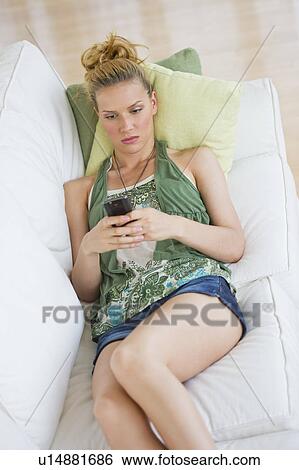 Stock Photograph - Woman lying on sofa and text messaging. Fotosearch