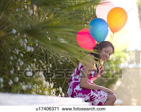 Young smiling woman sitting on wall and holding balloons View Large Photo Image Stock Image - Young smiling woman sitting on wall and holding balloons. Fotosearch