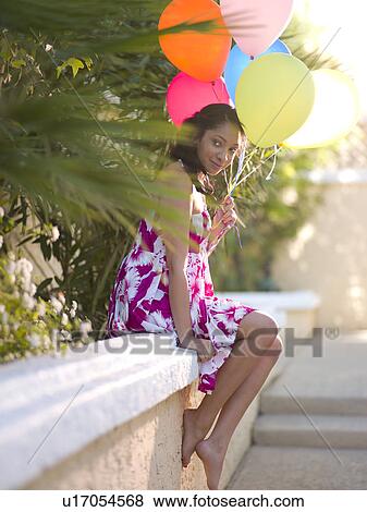 Young smiling woman sitting on wall and holding balloons View Large Photo Image Stock Photo - Young smiling woman sitting on wall and holding balloons. Fotosearch