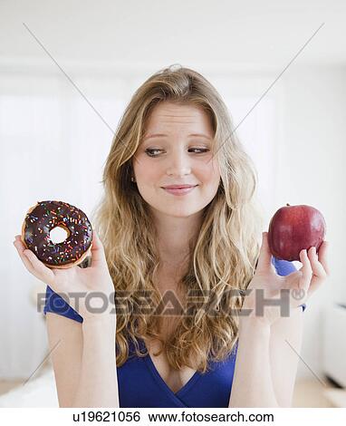 Young woman choosing between donut and apple View Large Photo Image Stock Photograph - Young woman choosing between donut and apple. Fotosearch