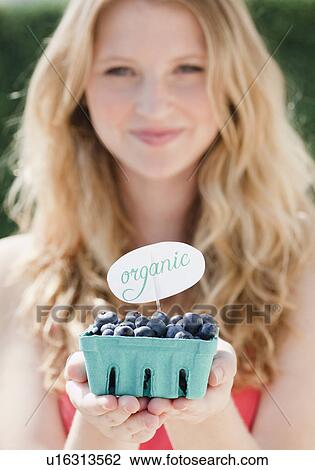 Stock Image - Young woman holding carton with organic blueberries. Fotosearch