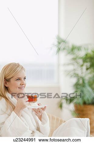 Stock Image - Young woman in bathrobe drinking tea. Fotosearch