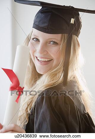 Stock Photo - Young woman wearing graduation gown with diploma. Fotosearch